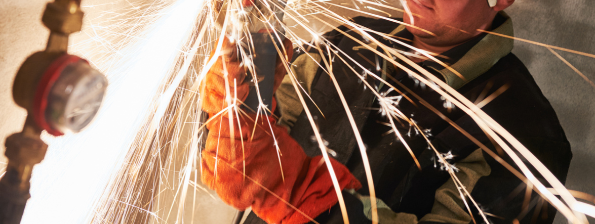 Worker cutting metal with sparks flying, wearing protective workwear fabric for safety